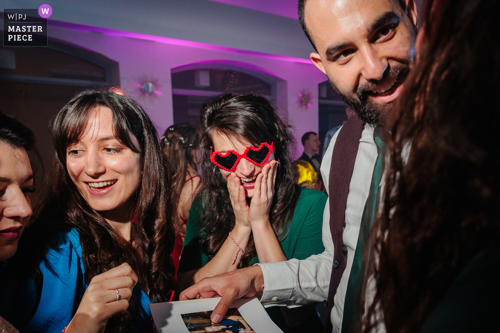 Un invité regarde le livre photo des mariés avec des lunettes cœurs, photo prise par Florian Fauvarque photographe de mariage. Élu WPJA Master Piece Purple par WPJA
