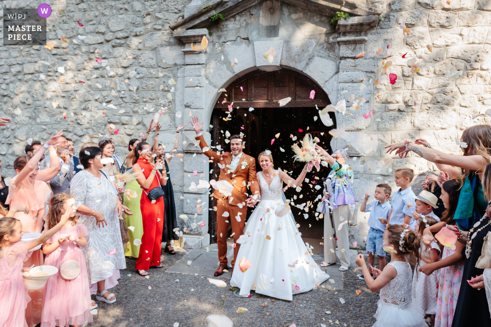 Les mariés sorte de l'église sous une pluie de pétales de fleurs, photo prise par Florian Fauvarque photographe de mariage. Élu WPJA Master Piece Purple par WPJA