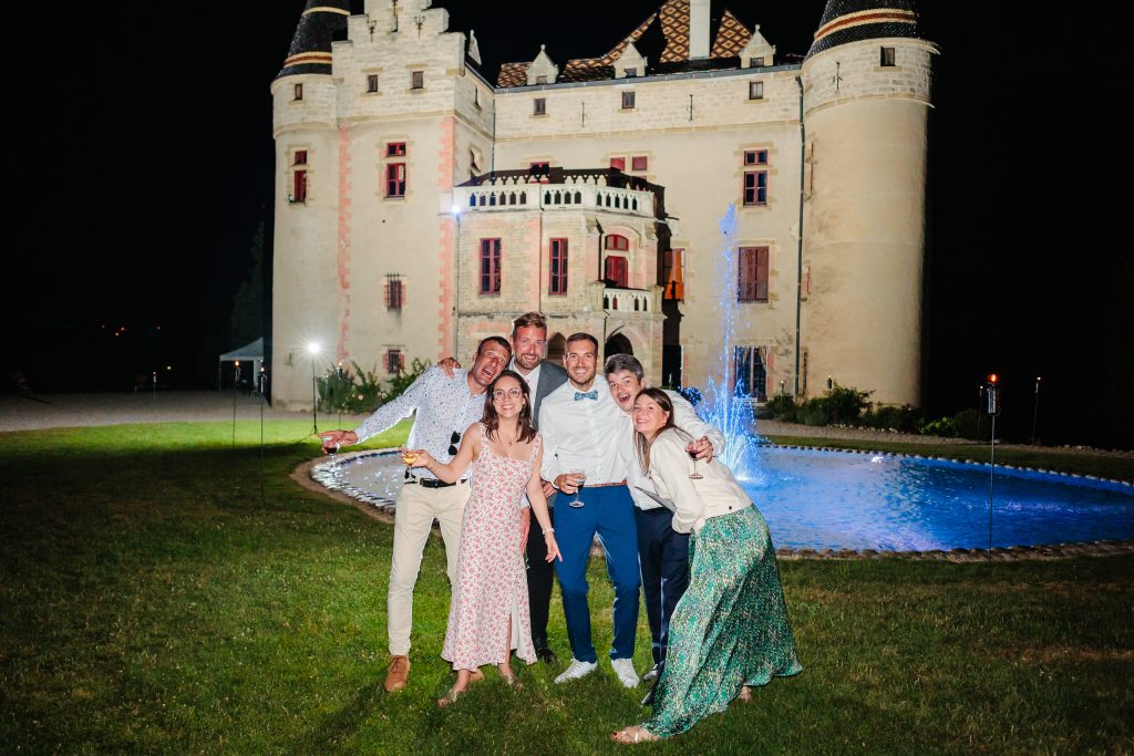 Groupe joyeux devant château magnifiquement éclairé la nuit, photo prise par Florian Fauvarque photographe de mariage à Grenoble et en Isère