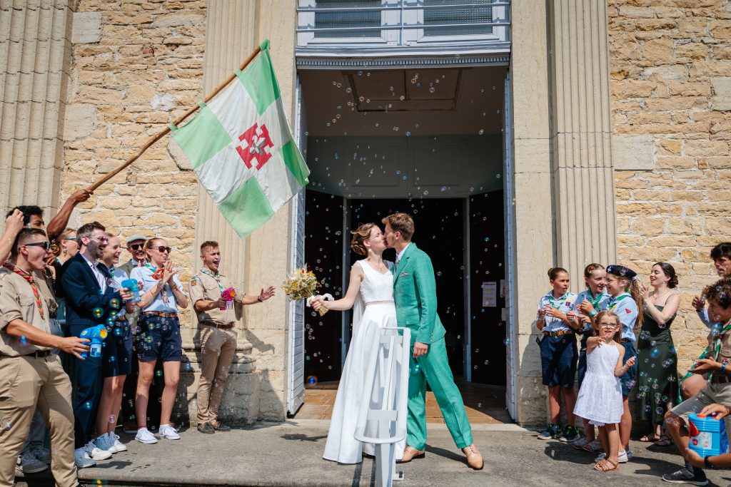 Couple de mariés s'embrassant à la sortie de l'église, Photo prise par Florian Fauvarque, photographe de mariage écoresponsable en Isère à Grenoble