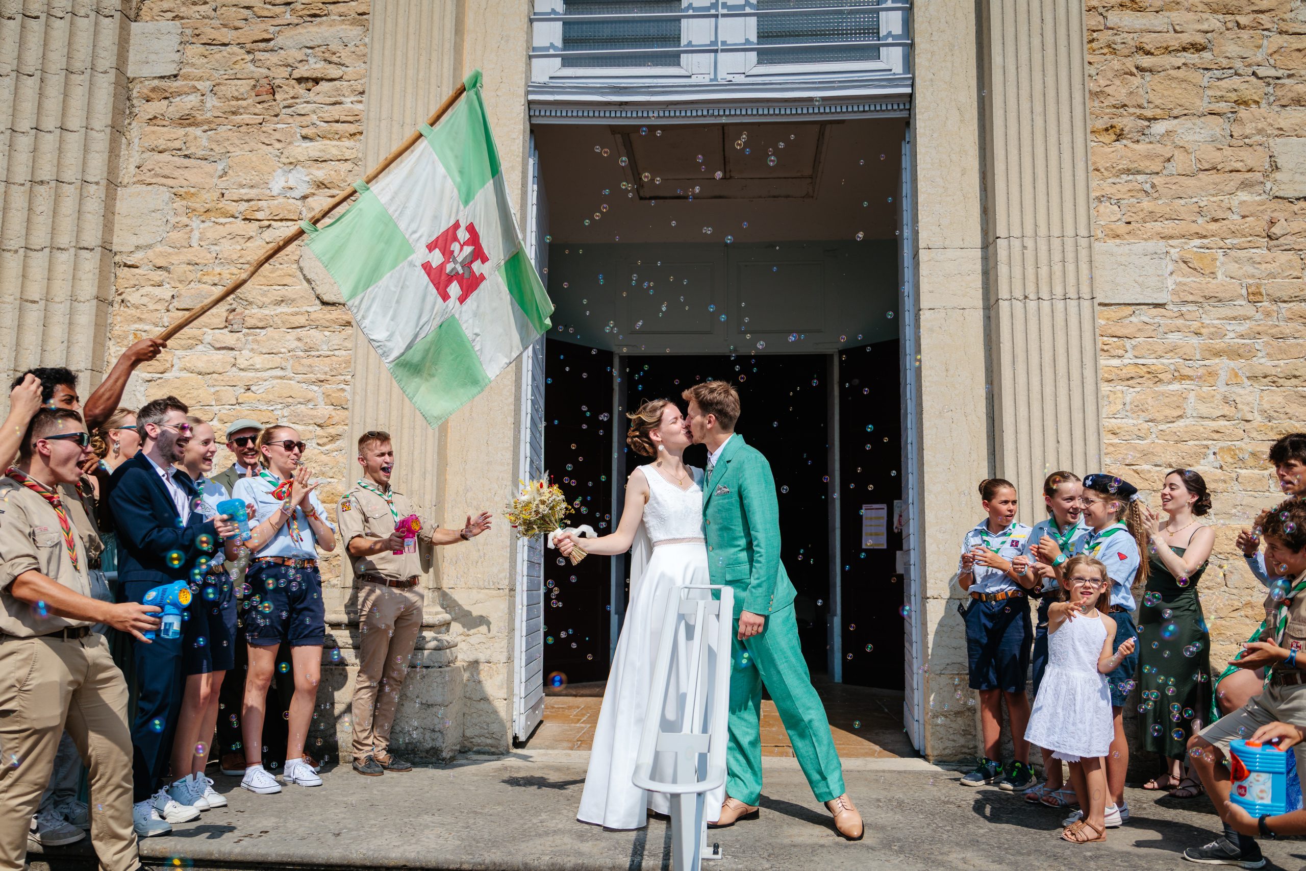 Couple de mariés s'embrassant à la sortie de l'église, Photo prise par Florian Fauvarque, photographe de mariage écoresponsable en Isère à Grenoble