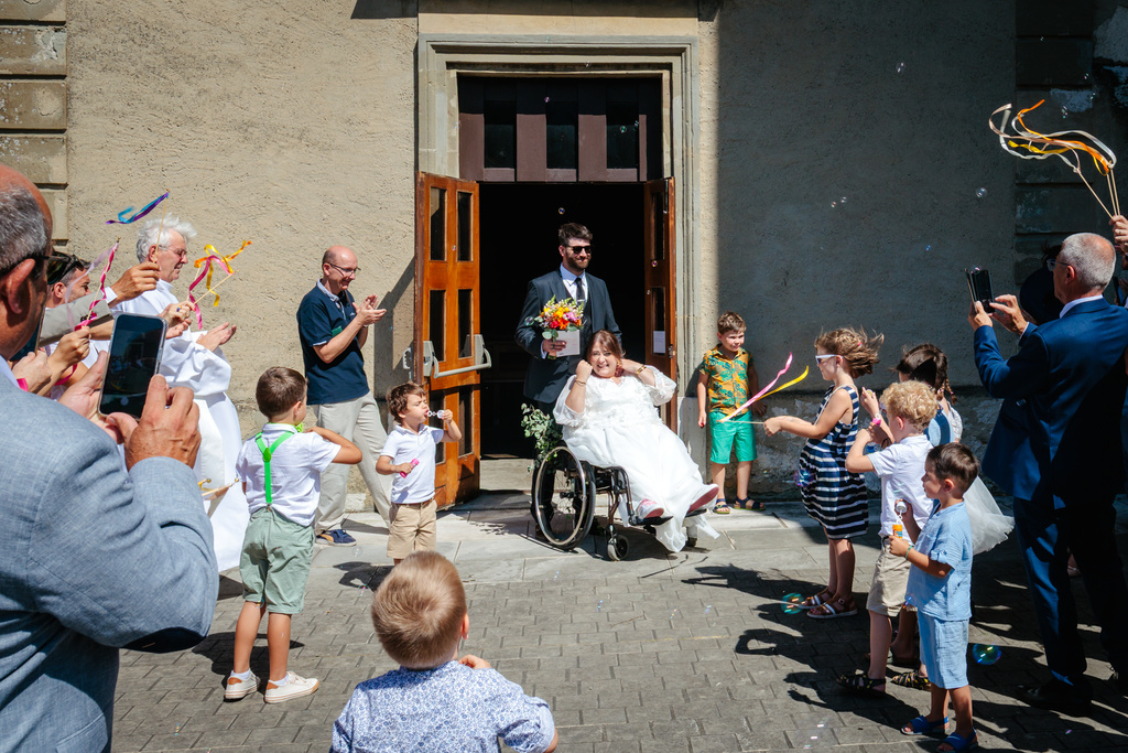 Sortie de cérémonie sous les bulles de savon en fauteuil roulant, photo prise par Florian Fauvarque photographe de mariage à Grenoble et en Isère