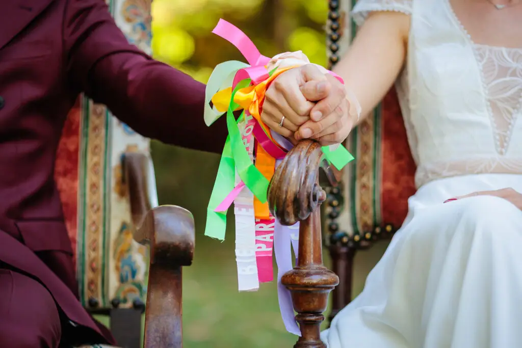 Mains de mariés liées par des rubans colorés, photo prise par Florian Fauvarque photographe de mariage à Grenoble et en Isère